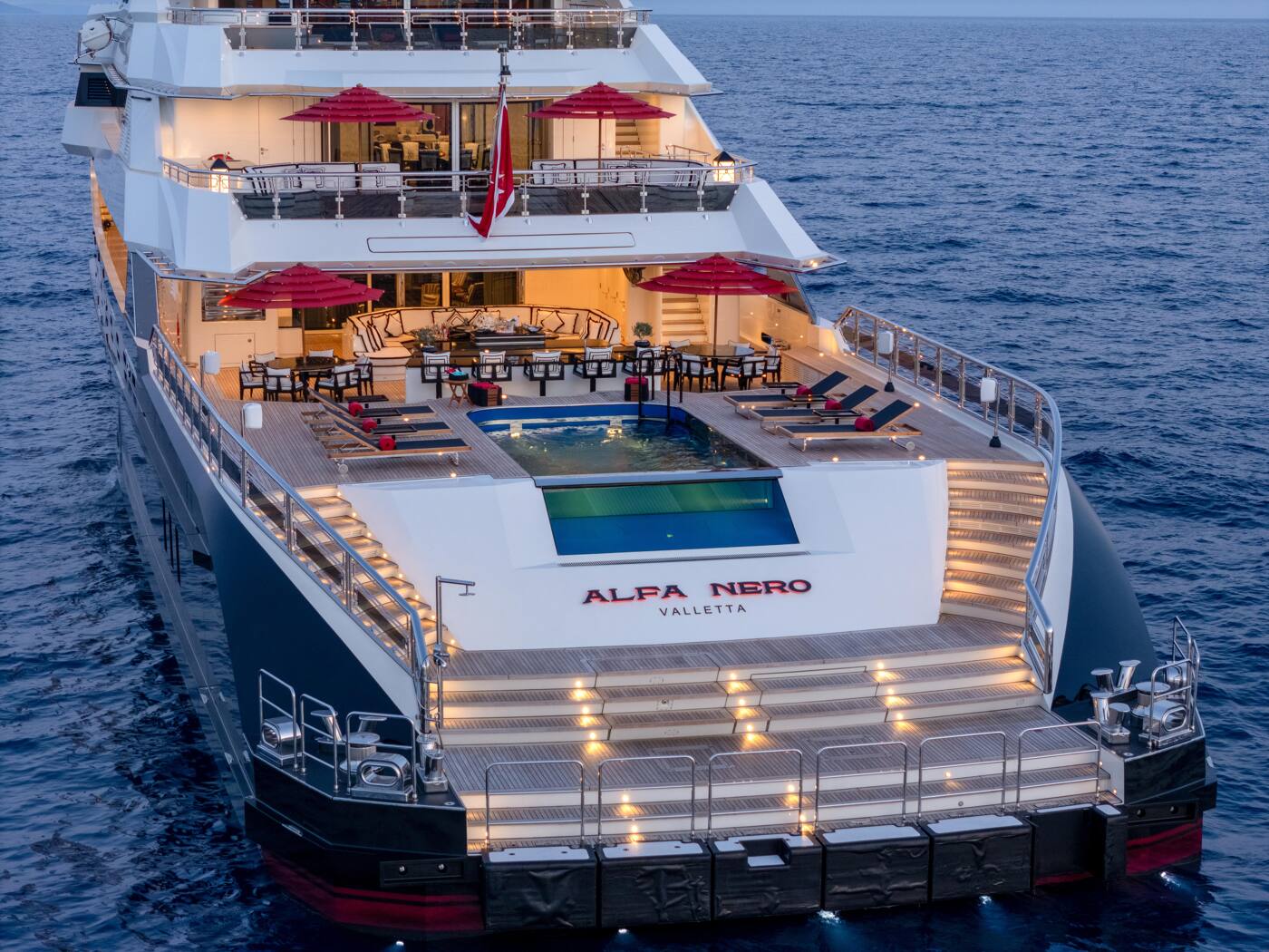 ALFA NERO photographed at dusk, her aft decks lit and the main deck pool glowing