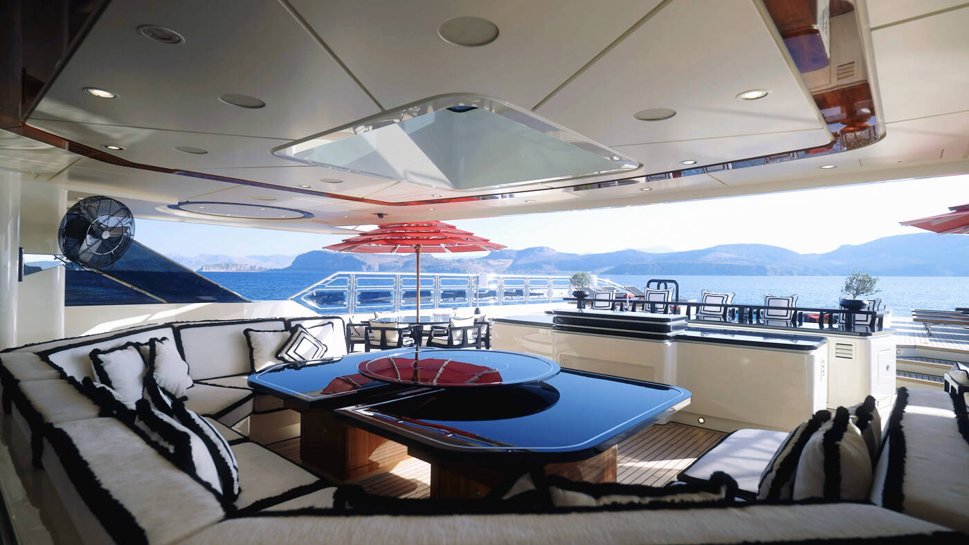 The covered upper deck aft aboard ALFA NERO, with banquette seating and a red parasol over the table