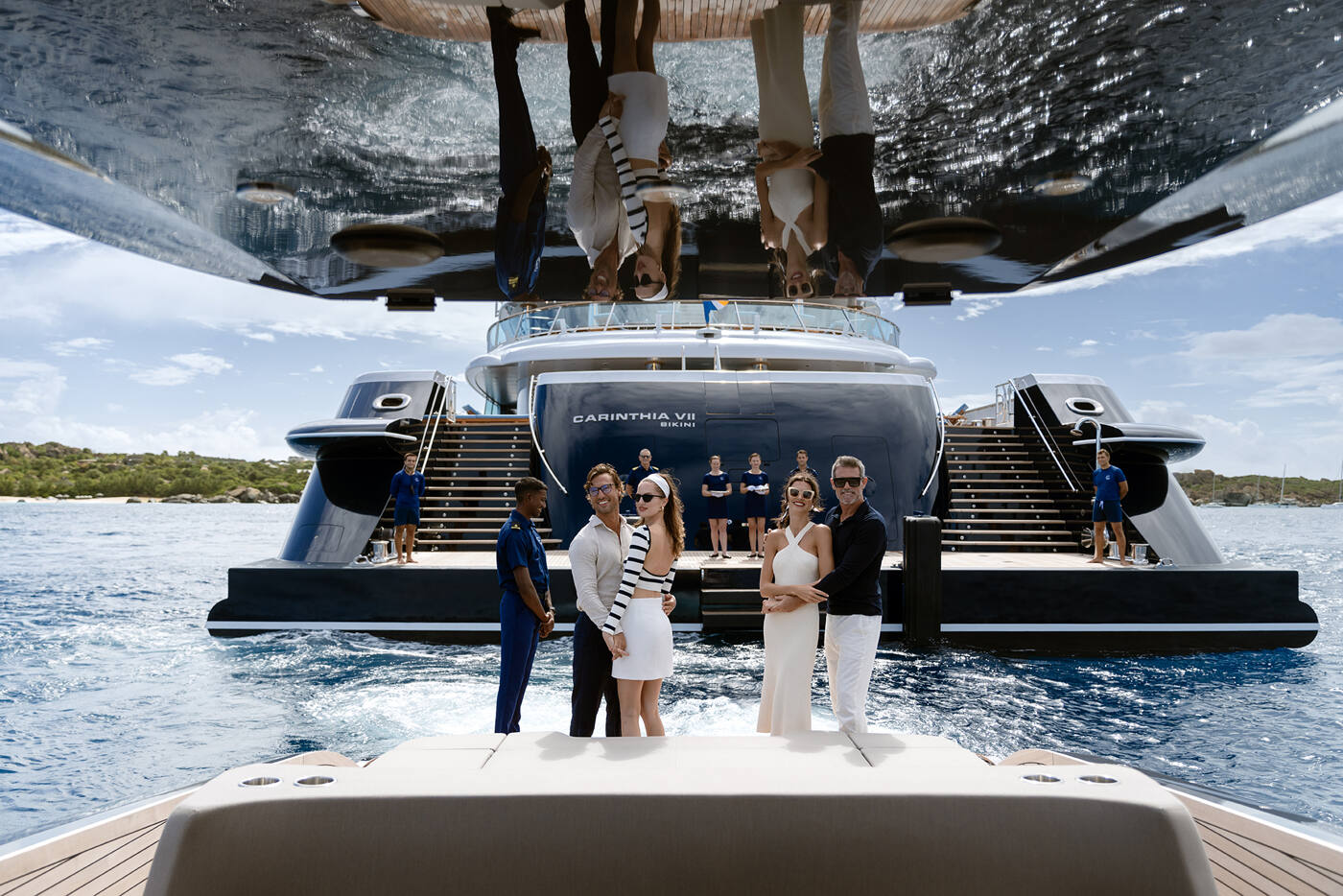 Guests and uniformed crew gathered on the teak swim platform of CARINTHIA VII, twin staircases sweeping up to the aft deck