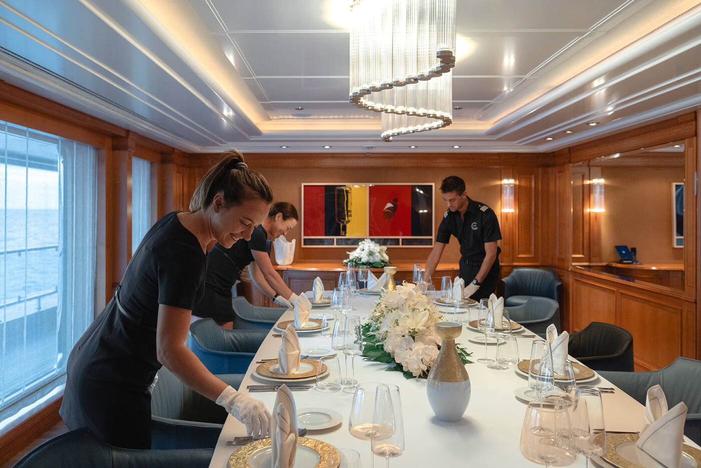 Two stewardesses and an officer laying the formal dining table in the wood-panelled dining salon of CARINTHIA VII