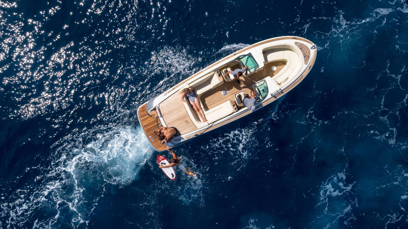 Aerial view of a tender under way with guests aboard and a paddleboarder alongside in deep blue water