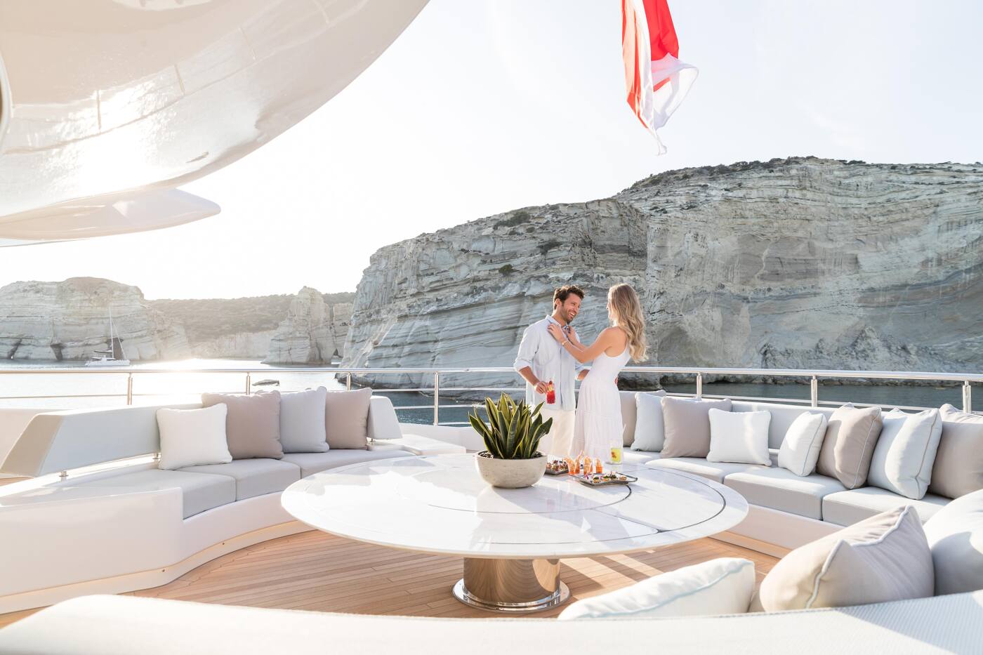 A couple with cocktails on the open sundeck lounge of O'PARI, white cliffs rising behind
